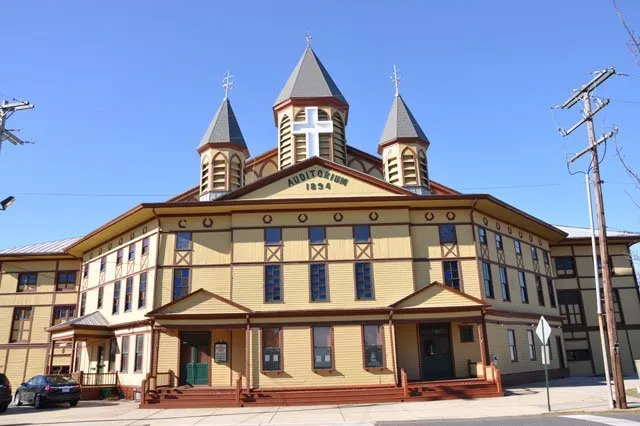 Historic building with three pointed towers and clock faces.